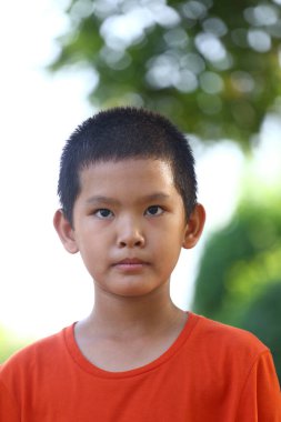 Kısa saçlı genç bir çocuk dışarıda duruyor, ciddi bir ifade sergiliyor. Arkaplan, çocukluk anılarının basitliğini vurgulayarak yeşilliği bulanıklaştırdı.