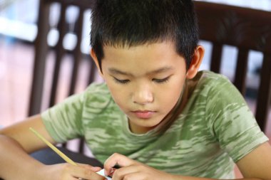 Evde yaratıcı bir işe konsantre olan genç bir çocuk. Odaklanmış ifadesi, öğrenmenin zevkini, pratik aktivitelerle yansıtıyor, hayal gücünü ve beceri gelişimini teşvik ediyor..