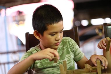 Genç bir çocuk ev içinde ahşap bloklarla inşa etmeye odaklanır, oyun sırasında yaratıcılığını gösterir ve odaklanır. Çocukluk sevinci ve öğrenme anı.