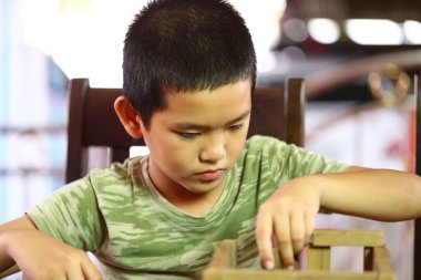 Genç bir çocuk içeride tahta bir oyuncakla oynamaya odaklandı. Konsantrasyonu çocukluk keşiflerinin ve günlük ortamdaki yaratıcılığın keyfini gösteriyor..