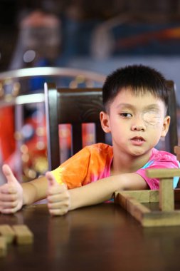 İfade dolu bir yüzü ve renkli gömleği olan genç bir çocuk bir masada oturur, hevesle tahta bloklarla oynar ve baş parmağını kaldırır, neşe saçar..