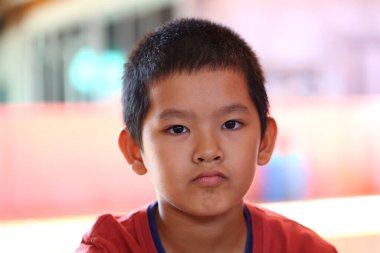 Ciddi bir ifadeyle çekilen düşünceli bir çocuğun portresi, canlı bir iç mekan ortamında düşünmeyi ve masumiyeti yansıtan samimi bir an sergiliyor..