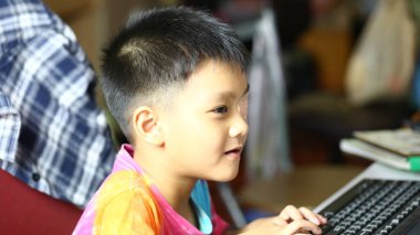 Küçük bir çocuk evdeki bir bilgisayara odaklanır, eğitim içeriğini araştırır. Bu ilgi çekici sahne, rahat bir ortamda modern öğrenmenin altını çiziyor..