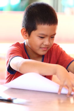 Genç bir çocuk masadaki yaratıcı bir aktiviteye derinden odaklanır. Konsantrasyonunu ve öğrenme yeteneğini kapalı alandaki kağıt işçiliğiyle gösterir..