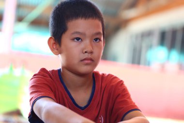 Ciddi bir ifadeye sahip genç bir çocuk hareketli bir ortamda oturur, derin bir odak ve tefekkür gösterir, çocukluk ve duygunun özünü yakalar..