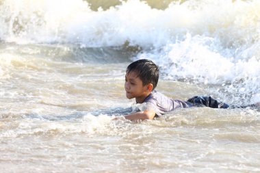 Genç bir çocuk neşeyle okyanus dalgalarında yüzüyor, güneşli bir plaj gününün neşesini ve heyecanını kucaklıyor, etrafını su sıçratıyor ve kaygısız bir atmosfer sarıyor..