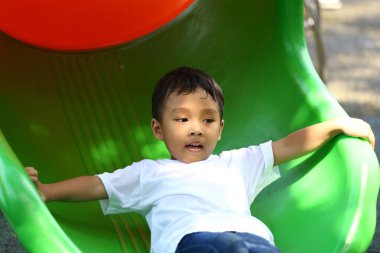 Neşeli bir çocuk oyun parkında hareketli bir kaydırağın üzerinde dinlenir, güneşi emer ve doğada eğlencenin ve kahkahanın tadını çıkarır..