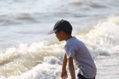 Genç bir çocuk kumsalda neşeli bir anın tadını çıkarıyor. Sahil kenarında hafif dalgalarla yürüyor. Parlak güneşli bir gökyüzünün altında, tasasız çocukluk sevincini somutlaştırıyor..