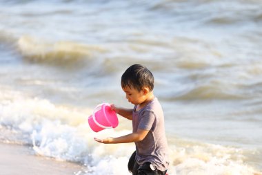 Elinde pembe bir kovayla kumsalda oynayan neşeli bir çocuk, su sıçratan dalgaların ve ılık güneşin tadını çıkarıyor, çocukluğun kaygısızca eğlencesini somutlaştırıyor..