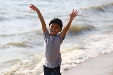 Güneşli bir günde çocukluk ruhunu somutlaştıran dalgalar onu sardığında kollarını kaldırıp sahilde neşeyle oynayan genç bir çocuk..
