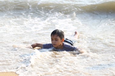 Genç bir çocuk, okyanus dalgalarında oynamanın, güneşin sıcaklığını kucaklamanın ve sahilde çocukluk macerasının heyecanını yaşıyor..