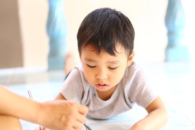 Genç bir çocuk, sanatsal büyümeyi destekleyen sıcak ve besleyici bir ortam sergileyerek, ebeveyninin rehberliğiyle yerde çizim yaparak yaratıcılığını ifade eder..