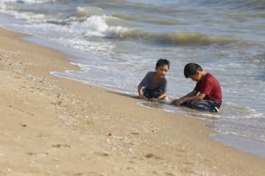 İki genç çocuk kumsalda keyifli bir anı paylaşıyor, kumsalda oynuyor ve güneşli bir günde hafif dalgalarda su sıçrıyor..