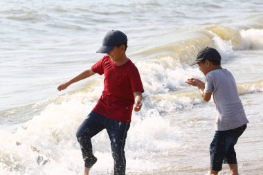 İki çocuk kumsalda neşeli bir anın tadını çıkarıyor, güneşin altında hafif dalgalar halinde, çocukluk sevincini ve doğanın güzelliğini kucaklıyor..