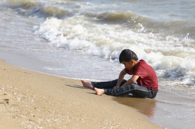 Küçük bir çocuk kumlu sahilde oturur, hayatı düşünür, dalgalar kıyıya vururken..