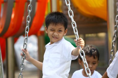 Neşeli genç bir çocuk oyun alanında sallanmaktan zevk alıyor, heyecan ve enerji sergiliyor. Neşeli ruhu çocukluk maceralarının özünü canlı bir ortamda yakalıyor..