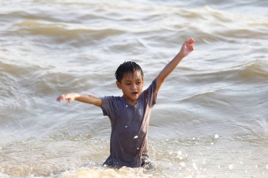Neşeli bir çocuk sahildeki sığ sulara sıçrıyor, yazı heyecan ve tasasız enerjiyle kucaklıyor, çocukluk sevinci ve maceranın özünü yakalıyor..