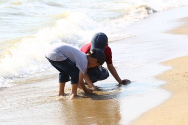 İki genç çocuk kumsalda kumla oynarken dalgalar nazikçe ayaklarının dibinde yuvarlanırken çocukluklarının kaygısız ruhunu ve açık hava maceralarının neşesini somutlaştırıyor..
