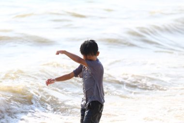 Küçük bir çocuk, sığ okyanus suyunda oynayarak kumsalda güneşli bir günün tadını çıkarıyor. Dalgalar neşeli bir sahne yaratır, tasasız çocukluk sevincinin özünü yakalar..