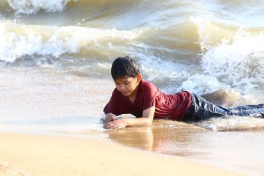 Genç bir çocuk sahilde eğlenceli bir gün geçirir, sığ sularda oynar ve nazik dalgalar ve ılık güneş ışığı altında doğanın keyfine varır..