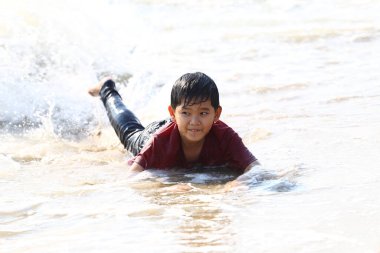 Neşeli bir çocuk sahildeki dalgalarda oynar, yaz eğlencesinin ve kaygısız anların ruhunu somutlaştırır. Çocukluk keyfi ve açık hava maceraları için mükemmel bir tasvir..
