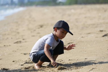 Genç bir çocuk, güzel bir sahilde yumuşak kumla etkileşime girer. Çocukluk neşesinin, merakının ve güneşin altındaki açık hava keşiflerinin özünü yakalar..
