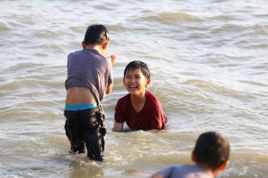 Bir grup neşeli çocuk sahilde sığ sularda oynuyorlar, birbirlerine su sıçratıyorlar ve gülüyorlar, yaz eğlencesinin ve çocukluk özgürlüğünün özünü yakalıyorlar..