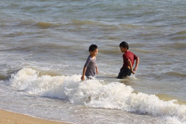 İki çocuk sahilde eğleniyor, sığ dalgalarda oynuyorlar, kahkaha, arkadaşlık ve yaz güneşinin sıcaklığıyla dolu canlı bir sahne yaratıyorlar..