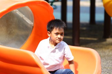 Neşeli genç bir çocuk turuncu bir oyun parkında güneşli bir günün tadını çıkarıyor. Bu görüntü, aile temalı projeler için mükemmel olan çocukluk eğlencesi ve macerasının özünü yansıtıyor..