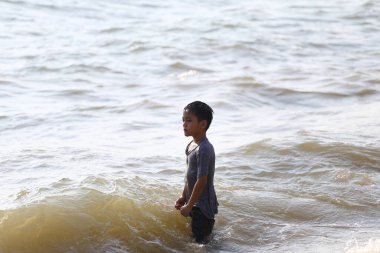 Genç bir çocuk sığ sularda duruyor, nazik dalgaların arasında neşeli anların tadını çıkarıyor, güneşli bir sahilde çocukluğun kaygısız ruhunu yansıtıyor..