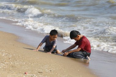 İki genç çocuk sahilde keyifli bir günün tadını çıkarıyorlar sığ sularda su sıçratıyorlar ve kumu kazıyorlar, huzurlu bir ortamda çocukluk sevincinin özünü yakalıyorlar..