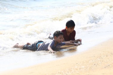 İki çocuk kumsalda uzanır. Dalgalar vücutlarına doğru kıvrılır gibi oynarlar. Sahne, güneşli bir günde deniz kenarında neşeli bir çocukluğun özünü yakalar..