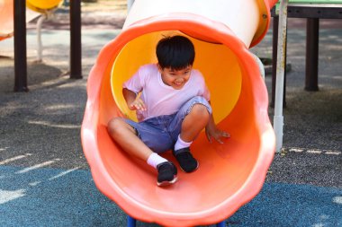 Genç bir çocuk, eğlenceli ve güneşli bir ortamda çocukluk neşesinin ve aktif oyunun özünü yakalayan canlı bir oyun parkından kayarak kaymayı seviyor..