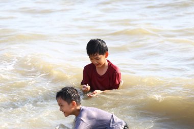 Güneşli bir yaz gününde hafif dalgalarla çevrili iki neşeli erkek çocuğu, çocukluk eğlencesi ve macerasının özünü yakalıyorlar..