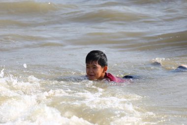 Genç bir çocuk güneşli bir plaj gününde neşe ve macerayı somutlaştıran narin okyanus dalgalarında yüzer. Kaygısız çocukluğun ve neşeli keşiflerin özünü yakalıyorum..