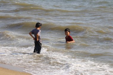 Sıcak güneşin altında neşeli ve neşeli bir atmosfer yaratan, çocukluk masumiyeti ve arkadaşlığı somutlaştıran, kumlu bir sahildeki sığ okyanus suyuna neşeyle sıçrayan iki genç çocuk..
