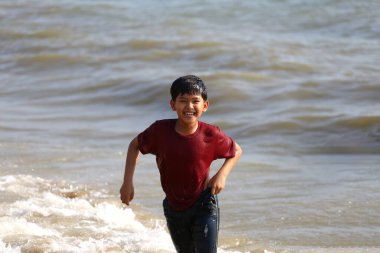 Neşeli genç bir çocuk sahilde neşeyle koşar, dalgaların arasından sıçrar ve parlak güneşin altında tasasız çocukluk anılarının özünü yakalar..