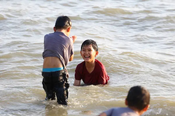 Bir grup neşeli çocuk sahilde sığ sularda oynuyorlar, birbirlerine su sıçratıyorlar ve gülüyorlar, yaz eğlencesinin ve çocukluk özgürlüğünün özünü yakalıyorlar..