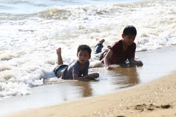 İki çocuk kumsalda neşeyle oynuyorlar, kumsalda yuvarlanıyorlar ve narin okyanus dalgalarında su sıçratıyorlar, çocukluk ruhunu sergiliyorlar..
