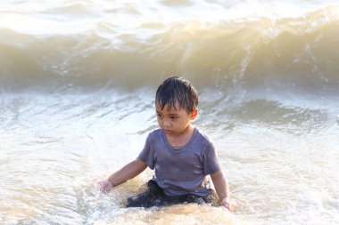Küçük bir çocuk sığ okyanus suyunda oynamaktan zevk alır, dalgaların neşesini keşfeder ve aydınlık bir yaz gününde, çocukluk anılarının güzelliğini vurgular..