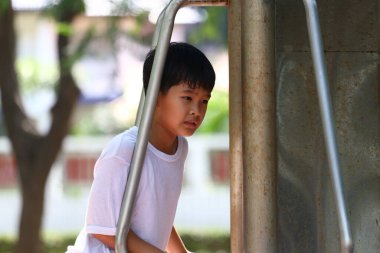 Parlak ve güneşli bir günde çevresi doğa ile çevrili bir şekilde tırmanırken kararlı ve odaklanmış bir şekilde oyun alanında oynayan genç bir çocuk..