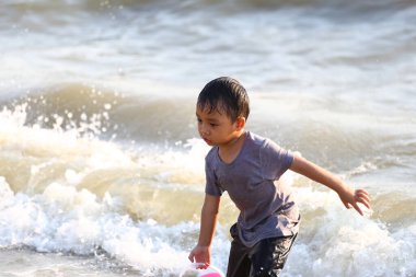 Genç bir çocuk sahilde oynuyor, neşe ve merakla dalgalarda yüzüyor. Bu görüntü çocukluk eğlencesinin özünü ve sahildeki bir günün güzelliğini yansıtıyor..
