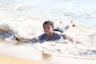 Genç bir çocuk sahildeki okyanus dalgalarında mutlu bir şekilde oynuyor, sıcak güneşin ve neşeli suyun tadını çıkarıyor, çocukluk ve açık hava eğlencesinin neşesini somutlaştırıyor..
