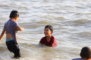 Çocuklar sahilde neşeli bir günün tadını çıkarıyorlar, sığ sulara sıçrayıp birlikte gülüyorlar, neşe ve gençliğin masumiyetini yakalıyorlar..