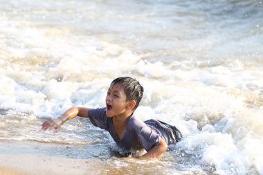 Neşeli bir çocuk sahildeki sığ sularda neşeyle oynar, dalgalarda su sıçratır ve güneşli bir günde çocukluğun saf zevkini sergiler..