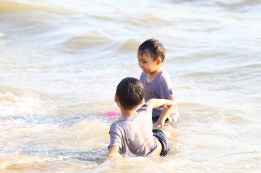 İki genç çocuk, sığ sularda çocukluk sevincini ve yaz eğlencesini sıcacık güneş ışığı altında yakalıyorlar..