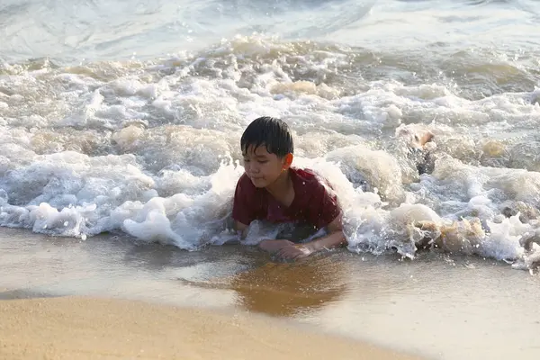 Sahildeki okyanus dalgalarının tadını çıkaran genç bir çocuk, su sıçratan su ve sıcak güneş ışığı arasında neşeli bir keşif ve neşe anı yakalıyor..