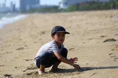 Genç bir çocuk güneşli bir plajda kumsalda oynamanın mutluluğunu yaşıyor, doğanın güzelliğinin tadını çıkarırken çevresinin dokusunu keşfediyor..