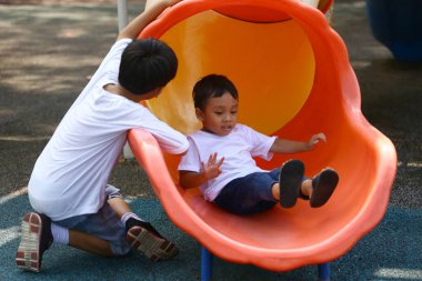 İki genç çocuk oyun bahçesinde renkli bir slaytta neşeyle oynuyorlar, açık havada çocukluk mutluluğunun ve maceranın özünü yakalıyorlar..