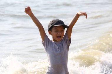 Neşeli bir çocuk kumsalda neşeyle oynuyor sığ sularda elleri havada sıçrıyor. Sahne, yazın özünü ve tasasız çocukluk hazzını yakalar..